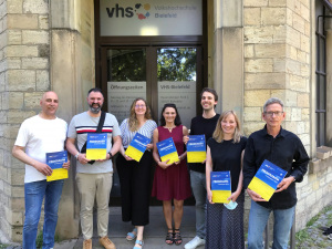 Vier Männer und drei Frauen halten das neue Programm der Volkshochschule, das als Broschüre erschienen ist, in die Höhe.